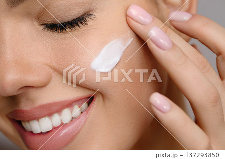 Woman with beautiful face touching healthy facial skin portrait. Beauty close up girl is applying a skincare product. Hydration. Cream smear Woman with beautiful face touching healthy facial skin portrait. Beauty close up girl is applying a skincare product. Hydration. Cream smear 137293850