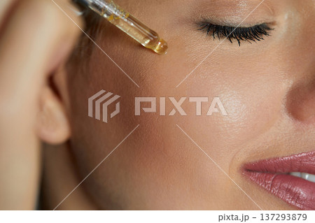 Serum. Moisturisg and nourishing. Close up beauty portrait of beautiful woman with glowing skin is applying a vitamin c skincare product with a pipette dropper.. Serum. Moisturisg and nourishing. Close up beauty portrait of beautiful woman with glowing skin is applying a vitamin c skincare product with a pipette dropper.. 137293879