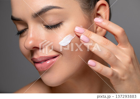 Skin care. Beauty close up portrait of young woman with a glowing skin is applying a cream smear. Skin care. Beauty close up portrait of young woman with a glowing skin is applying a cream smear. 137293883