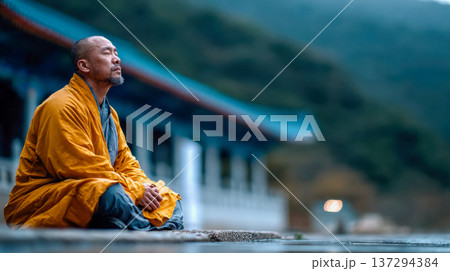 Buddhist monk meditating in lotus pose facing a misty mountain temple courtyard at dawn, peaceful spiritual retreat atmosphere 137294384