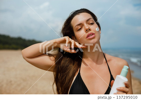 Beautiful woman applying sunscreen lotion on face at beach, summer skincare routine and sun protection concept with natural beauty and healthy skin Beautiful woman applying sunscreen lotion on face at beach, summer skincare routine and sun protection concept with natural beauty and healthy skin 137295010