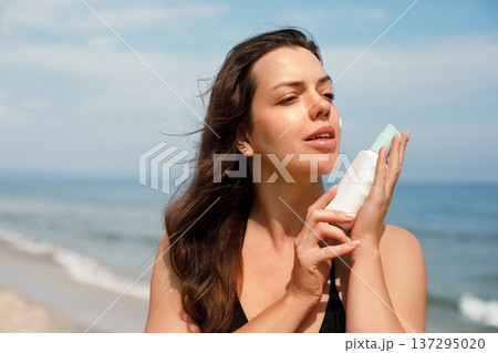 Attractive woman applying sunscreen lotion on cheek at beach under sunlight, skincare and UV protection concept Attractive woman applying sunscreen lotion on cheek at beach under sunlight, skincare and UV protection concept 137295020