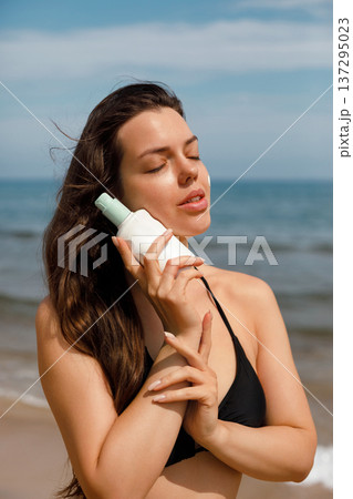 Close portrait of woman with sunscreen lotion bottle at beach, skincare and sun protection concept Close portrait of woman with sunscreen lotion bottle at beach, skincare and sun protection concept 137295023