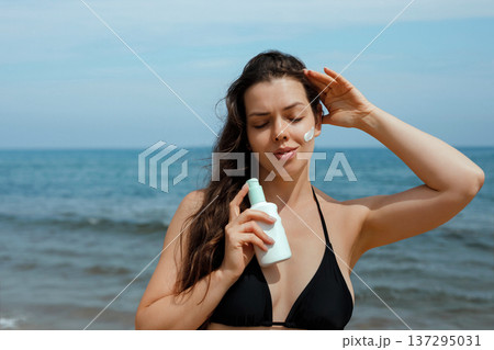 Smiling woman holding sunscreen suncream lotion and enjoying sunlight at beach, female using sunblock for healthy glowing skin 137295031