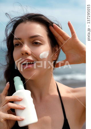 Close portrait of woman with sunscreen suncream lotion on face at beach, female using sunblock for skincare and UV protection 137295055