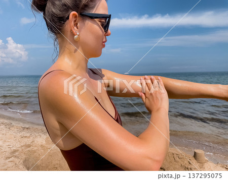 Woman applying sunscreen lotion on arm at beach, close up of summer skincare routine and sun protection concept with hydrated glowing skin Woman applying sunscreen lotion on arm at beach, close up of summer skincare routine and sun protection concept with hydrated glowing skin 137295075