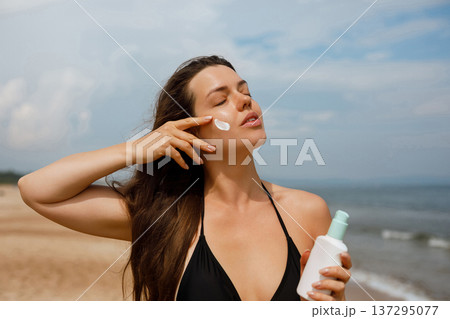 Young woman touching skin while holding sunscreen bottle at seaside, beauty skincare and sun protection concept with healthy glowing face Young woman touching skin while holding sunscreen bottle at seaside, beauty skincare and sun protection concept with healthy glowing face 137295077