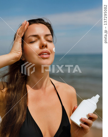 Young woman applying sunscreen lotion on upper body while holding bottle at seaside, summer skincare and sun protection concept with healthy lifestyle 137295082