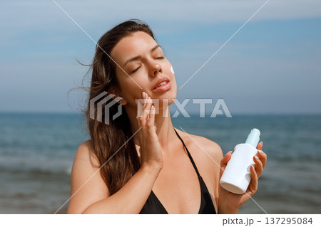 Close up of woman applying sunscreen on cheek using suncream lotion for skin protection at beach 137295084