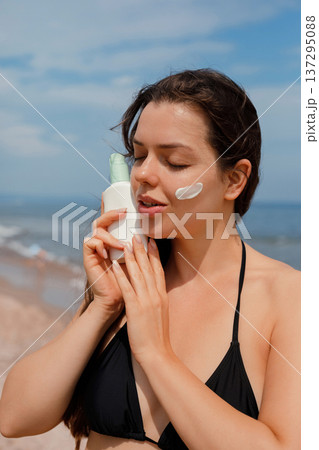 Woman gently applying sunscreen lotion on face at beach, skincare and sun protection concept Woman gently applying sunscreen lotion on face at beach, skincare and sun protection concept 137295088