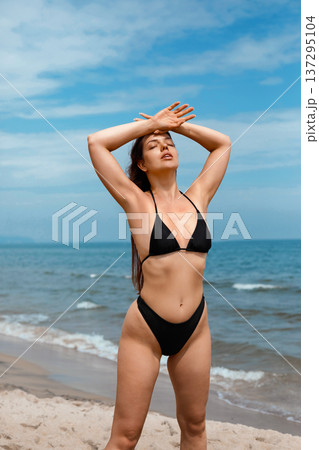 Attractive woman enjoying sunlight on beach in bikini raising arms and using sunscreen suncream lotion for UV protection skincare and summer wellness concept Attractive woman enjoying sunlight on beach in bikini raising arms and using sunscreen suncream lotion for UV protection skincare and summer wellness concept 137295104