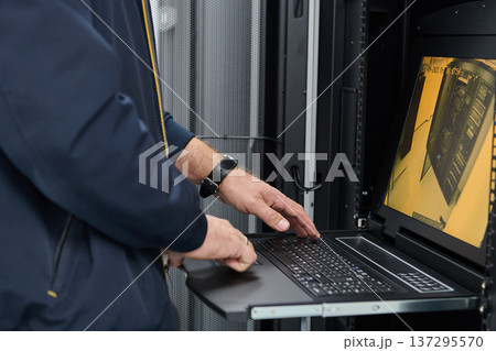 IT technician monitoring server rack on laptop in a data center during maintenance IT technician monitoring server rack on laptop in a data center during maintenance 137295570