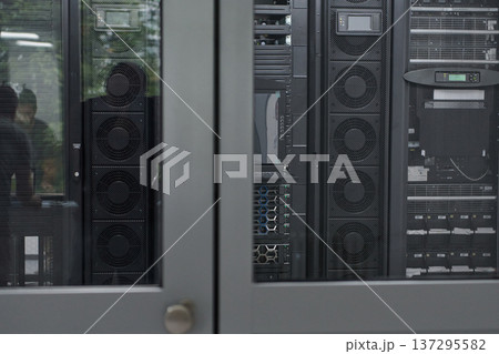 Engineers working in a secure data center with server racks visible through a glass door 137295582