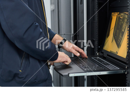 IT technician working on server rack using laptop console in data center for system maintenance and monitoring IT technician working on server rack using laptop console in data center for system maintenance and monitoring 137295585