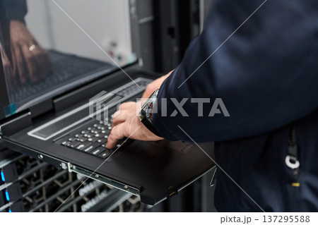 IT technician typing on a rack console laptop in a data center server room during maintenance IT technician typing on a rack console laptop in a data center server room during maintenance 137295588