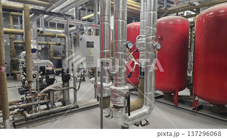 Interior view of industrial facility displaying red pressure tanks alongside metallic piping systems equipped with valves and gauges, highlighting sophisticated arrangement of machinery and equipment 137296068