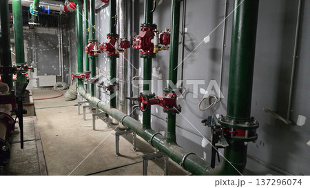 Industrial plumbing setup with green pipes and red valves arranged along a concrete wall in a construction area, showcasing tools and equipment positioned on the floor nearby 137296074