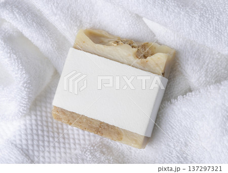Mockup of beige solid soap bar with blank paper label on white bath towel, personal care packaging 137297321