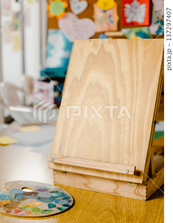 Portable wooden easel and paint palette on a table Portable wooden easel and paint palette on a table 137297407