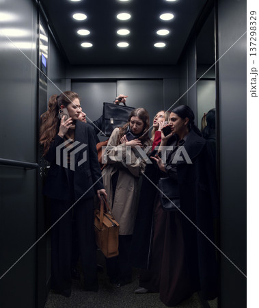 Group of businesswomen using smartphones while standing inside crowded office elevator. 137298329