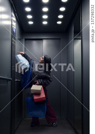 Woman with shopping bags pressing elevator button inside modern building elevator. Woman with shopping bags pressing elevator button inside modern building elevator. 137298332
