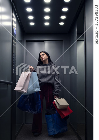 Young woman carrying shopping bags while standing in elevator after retail purchase 137298333