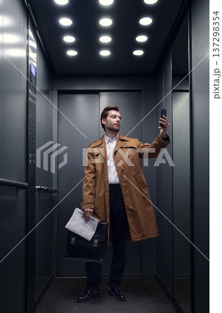 Businessman taking selfie with smartphone inside office elevator. 137298354