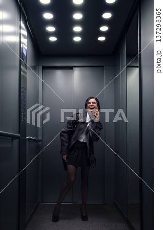 Young woman laughing while talking on smartphone inside modern elevator. Young woman laughing while talking on smartphone inside modern elevator. 137298365