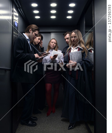 Group of business professionals using smartphones and tablets inside crowded office elevator Group of business professionals using smartphones and tablets inside crowded office elevator 137298393