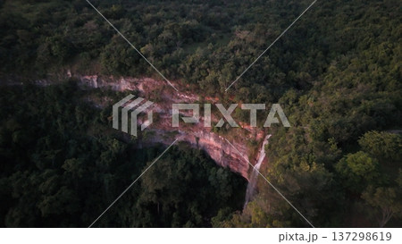 Cassilandia, Mato Grosso do Sul, Brazil - 04 05 2024. Drone aerial view of Cachoeira do Socorro waterfall flowing over a rocky cliff surrounded by dense forest vegetation during early morning light. Cassilandia, Mato Grosso do Sul, Brazil - 04 05 2024. Drone aerial view of Cachoeira do Socorro waterfall flowing over a rocky cliff surrounded by dense forest vegetation during early morning light. 137298619
