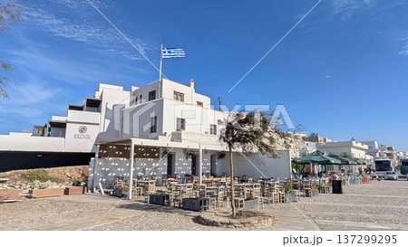 Touristic street and white buildings with Greek flags and open terrace restaurant under the blue sky Touristic street and white buildings with Greek flags and open terrace restaurant under the blue sky 137299295