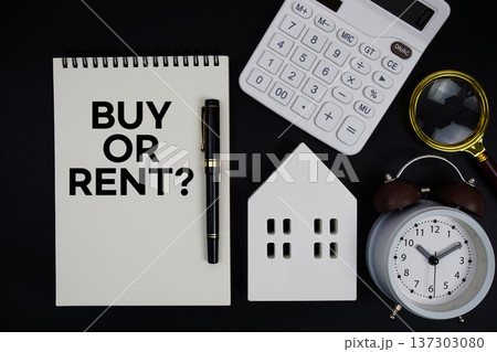 Notepad with the phrase "Buy Or Rent?" surrounded by a pen, calculator, magnifying glass, clock, and house model 137303080