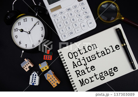 Notepad with the phrase "Option Adjustable Rate Mortgage" surrounded by a pen, calculator, magnifying glass, clock, and house model 137303089