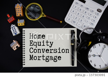 Notepad with the phrase "HECM Home Equity Conversion Mortgage" surrounded by a pen, calculator, magnifying glass, clock, and house model 137303091