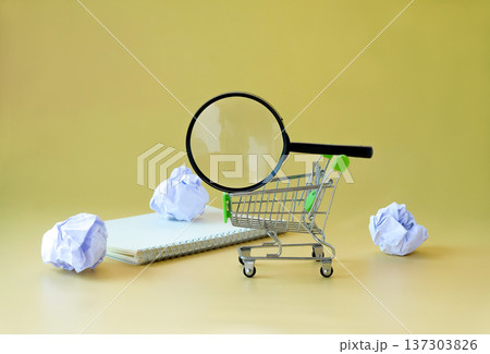 Magnifying glass on shopping cart and crumpled paper around. Magnifying glass on shopping cart and crumpled paper around. 137303826
