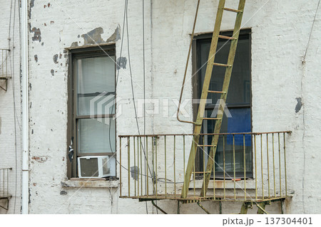 Close view of an older Manhattan residential building featuring a metal fire escape and window air conditioner. Weathered facade and urban details reflect classic New York City architecture. Close view of an older Manhattan residential building featuring a metal fire escape and window air conditioner. Weathered facade and urban details reflect classic New York City architecture. 137304401