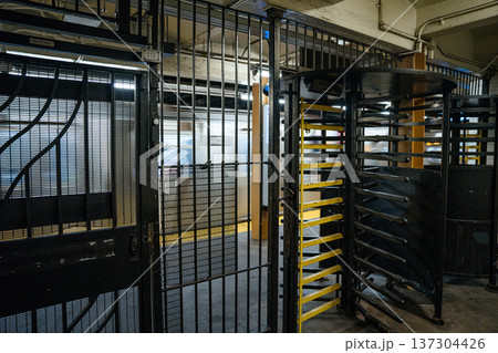 Metal turnstiles and security gates stand inside an underground subway station entrance. Blurred train movement in the background suggests active public transportation. 137304426