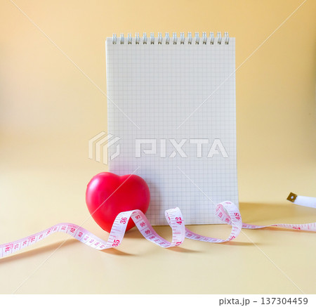 A booknote and red heart with measuring tape , healthcare concept. A booknote and red heart with measuring tape , healthcare concept. 137304459