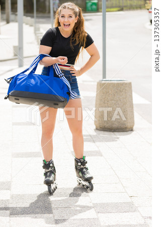 Young woman riding roller skates holding bag 137305357