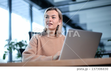 A woman is sitting at a desk with a laptop in front of her A woman is sitting at a desk with a laptop in front of her 137306830