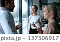Three people are standing in front of a window, smiling and holding cups 137306917