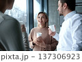 Three people are standing in front of a window, smiling and holding cups 137306923