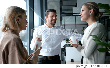Three people are standing in front of a window, smiling and holding cups 137306924