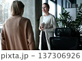 Two women are talking in a room with a potted plant in the background 137306926