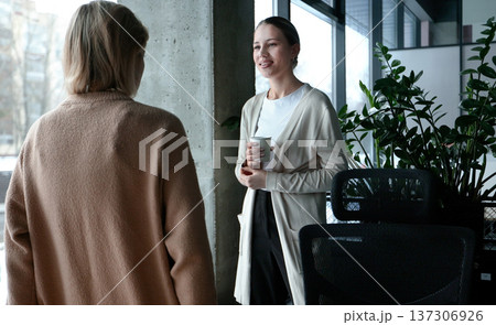 Two women are talking in a room with a potted plant in the background 137306926