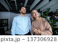 A man and a woman are standing in front of a plant 137306928