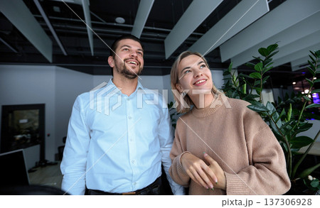 A man and a woman are standing in front of a plant 137306928