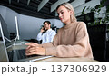 A woman is typing on a laptop while a man talks on the phone 137306929