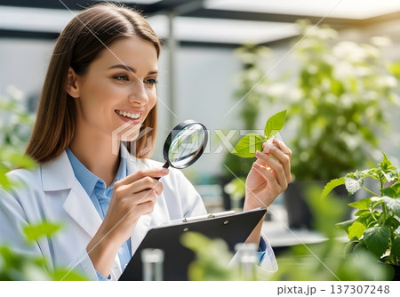 Smiling Female Biologist Examines Healthy Plant Leaf with Magnifying Glass in Greenhouse Laboratory 137307248