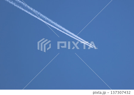 airplane flies across a clear blue sky, leaving twin white contrails airplane flies across a clear blue sky, leaving twin white contrails 137307432